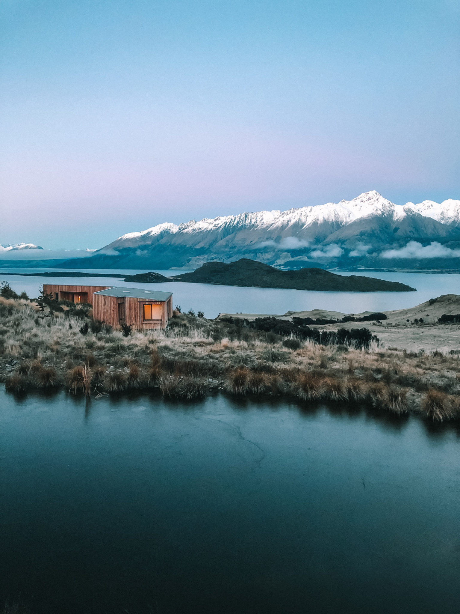 Aro Hā lodge beside an alpine tarn below snow-capped peaks, Glenorchy, New Zealand